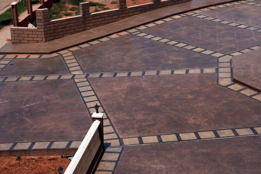 Aerial view of a decorative concrete patio with a geometric design and brick borders, featuring light posts and railing.
